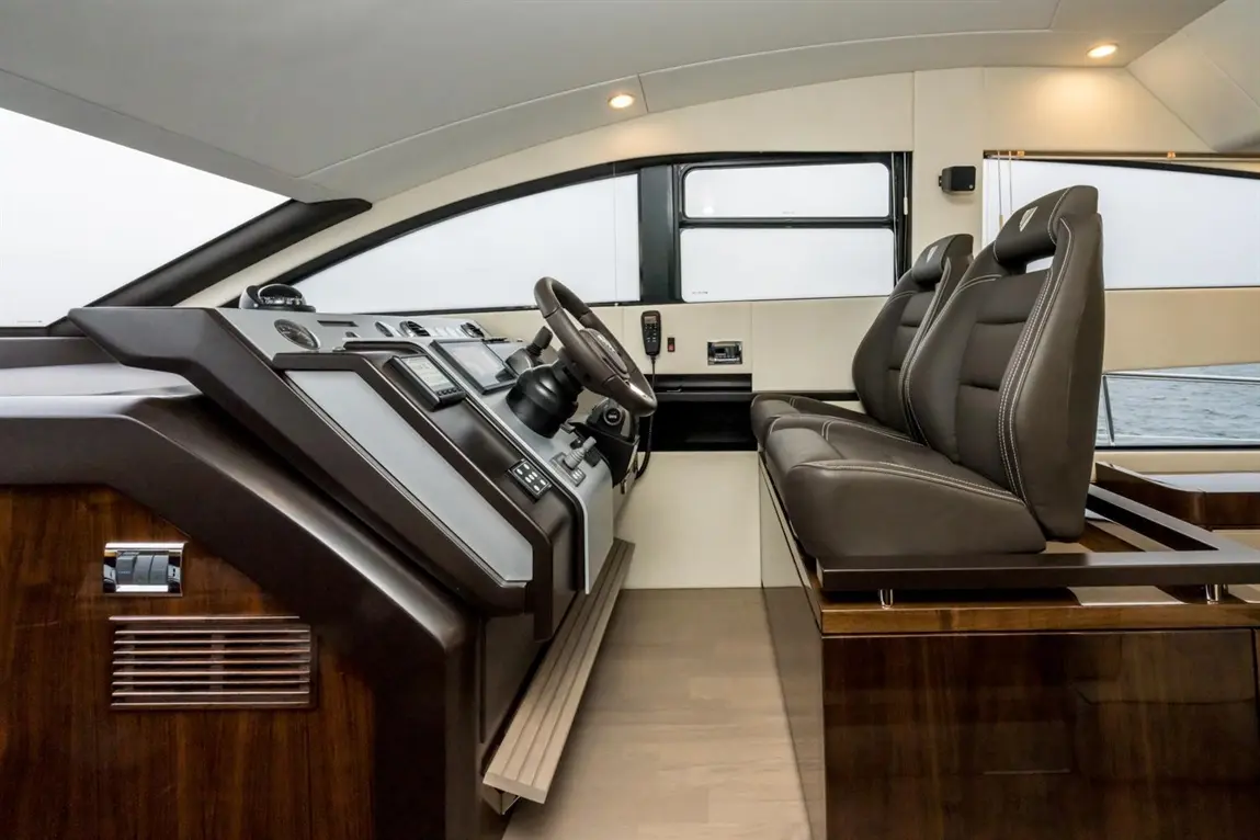 Luxury yacht interior with a steering wheel, control panel, and leather seating, featuring large windows for scenic views.